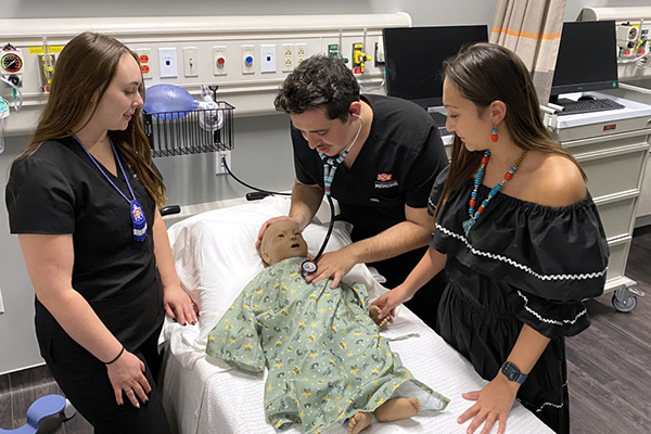Two female and one male Native American medical students listening to a simulated baby's heartbeat.