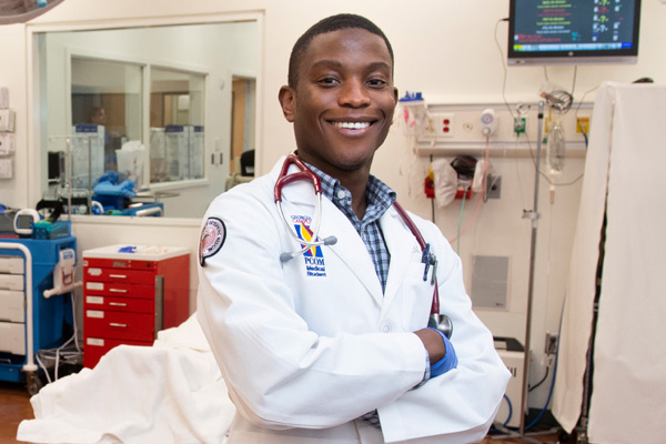 Smiling Black male medical student in whitecoat and stethoscope with arms crossed.