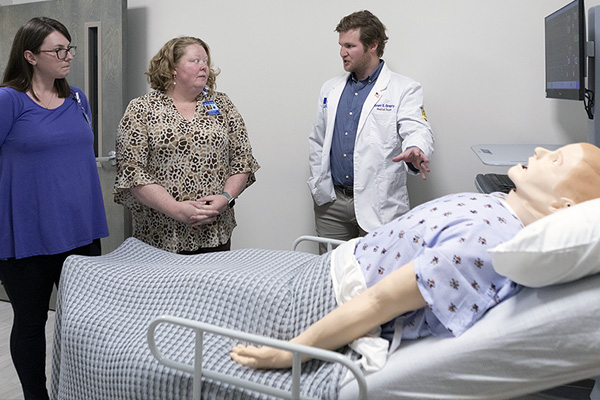 ACOM faculty and student discussing a simulated patient lying on a gurney