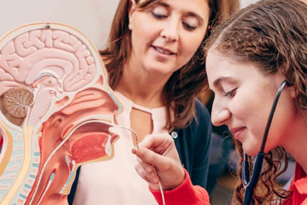Two female medical student practice inserting a tube down a plastic patient's throat.