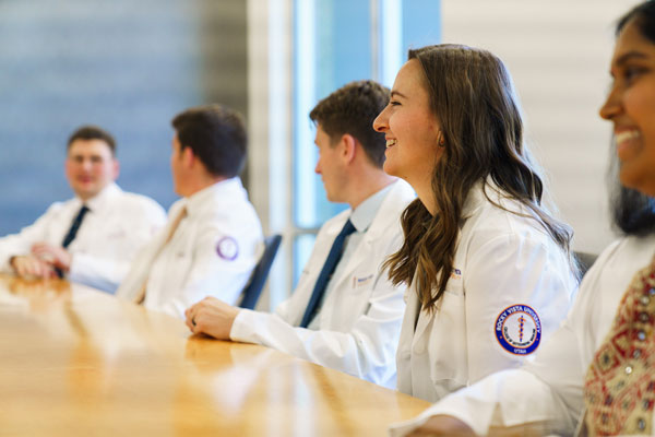 Smiling students in white coat sitting around a table.