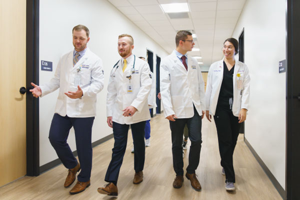 RVU-MCOM students in white coat walking together in a hallway.