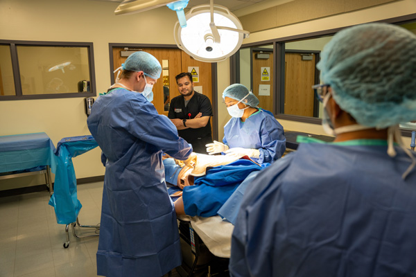 UIWSOM medical students in blue scrubs practice surgery on a simulated patient.