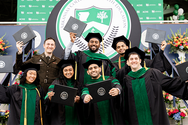 Smiling DO graduates in academic robes displaying their diplomas