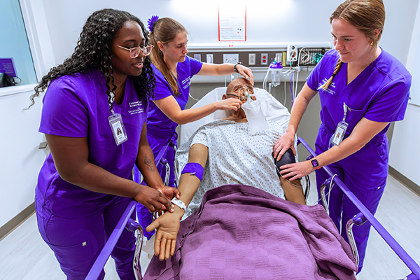 DMUCOM students practicing taking blood pressure, pulse and applying an oxygen mask on a patient on a guer