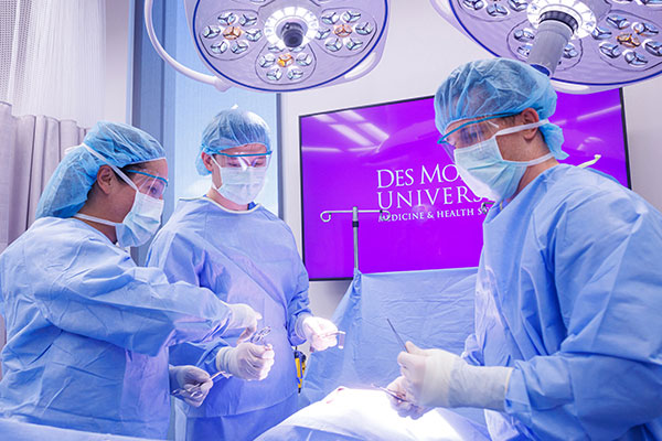 Students dressed in blue surgical garb examining tools in a surgical theater.