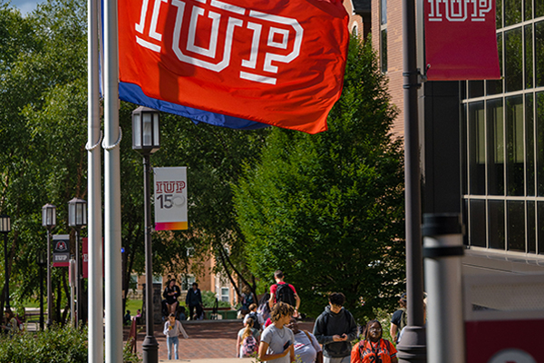 Red IUP flag blows in the breeze while students walk around campus on a sunny day