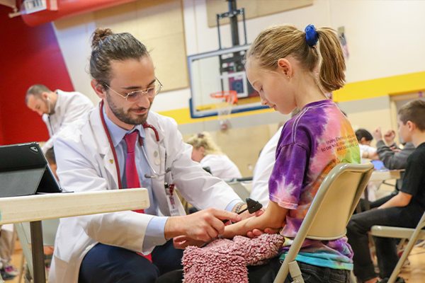 KCU-COM student in white coat checking a girl's reflexes at a school health fair