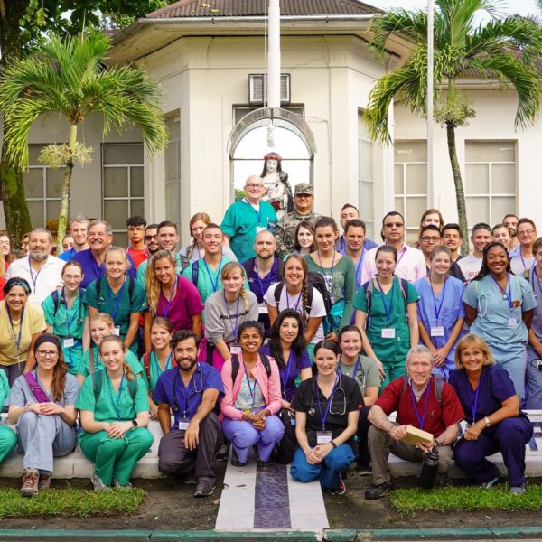 A group of students and faculty posing outside in their scrubs
