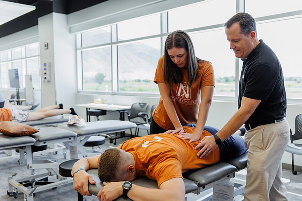 Instructor guiding DO student practicing OMM on the back of another student