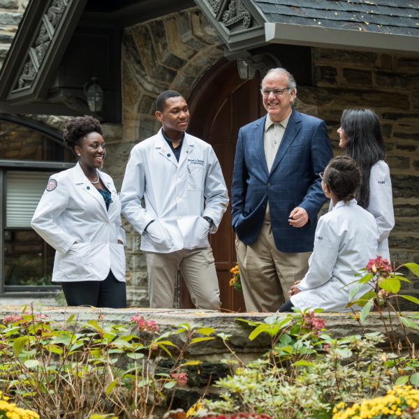 PCOM students in white coat speaking with a dean.