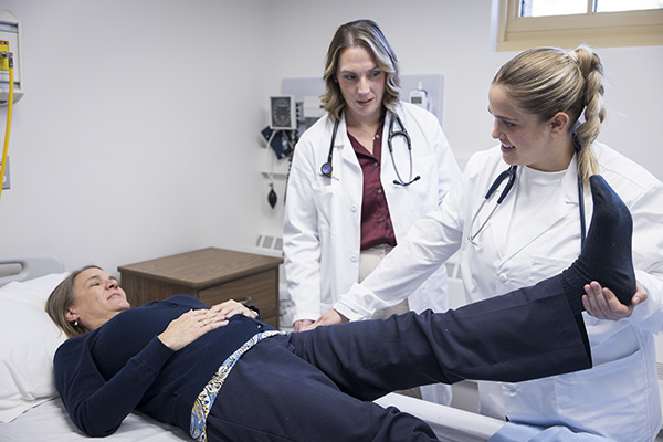 Female medical student examines a patient's hip joint while being observed by an instructor.