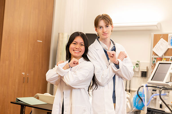 Two medical students in white coat smile for the camera.