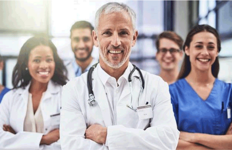 Five male and female doctors smile at the camera with arms crossed.
