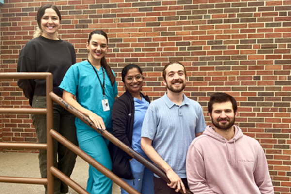 Five medical students stand on a staircase against a brick wall, smiling.