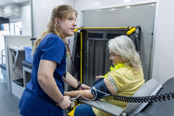 A healthcare worker in scrubs checks an older woman's blood pressure.