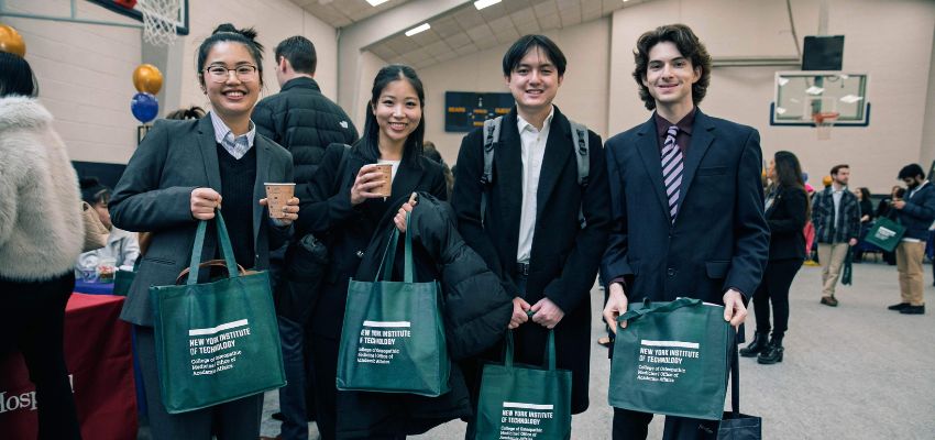 Four professionally-dressed students carry NYITCOM tote bags
