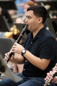 A musician plays a clarinet during a seated ensemble rehearsal.