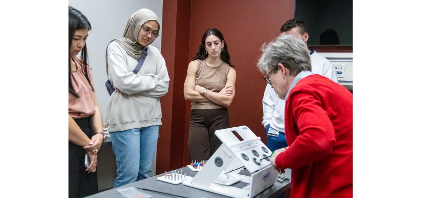Students observe an instructor demonstrating the use of medical equipment during a hands-on classroom session.