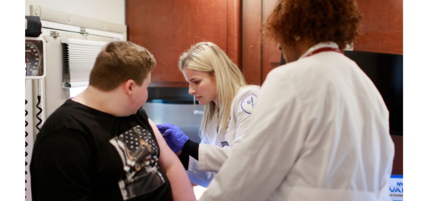 A medical student administers a vaccine to a young patient while a supervising physician observes.