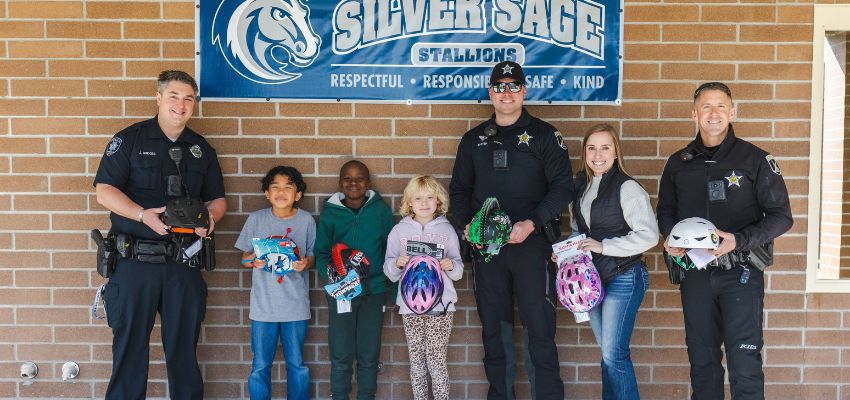 Police officers and children smile together while holding bike helmets beneath a banner that reads “Silver Sage Stallions.”