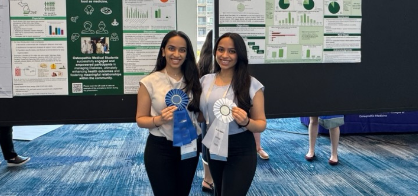 Two MSUCOM students stand in front of their research posters, smiling and holding award ribbons for their presentation achievements.