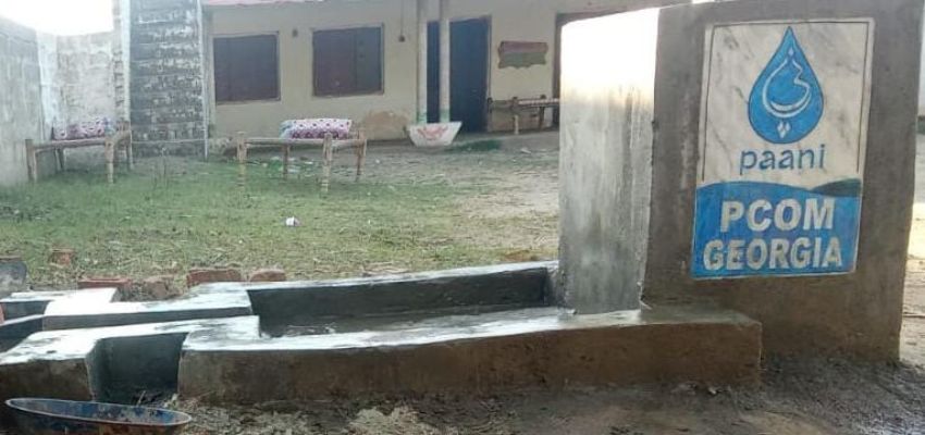 A clean water installation in a rural area is labeled “Paani” and “PCOM Georgia,” highlighting a global outreach effort.