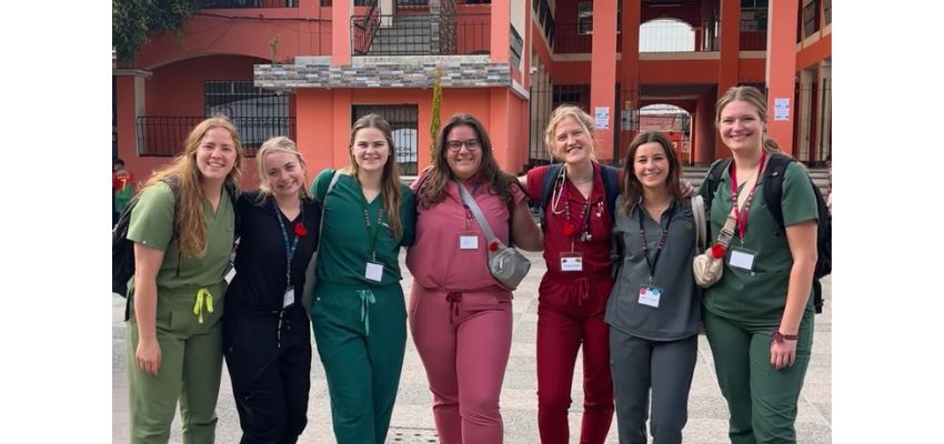 A group of seven students in scrubs pose for a photo together while on a medical outreach trip.