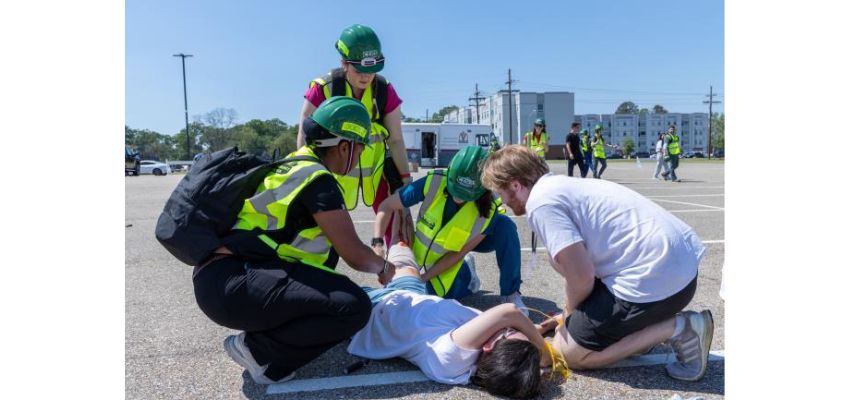 Emergency responders in safety vests assist a mock “injured” person on the ground during a disaster response training simulation.