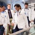 Sevenmedicalstudentsinwhitecoatswalkdownastaircaseinsideamodernacademicbuilding