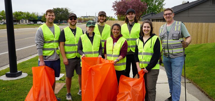 A group of Idaho College of Osteopathic Medicine (ICOM) students and staff in reflective vests hold orange garbage bags during a community cleanup activity.
