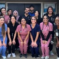 AgroupofUNTHSC-TCOMmedicalstudentsgatherinfrontofaclinicbuildingsmilingintheirscrubswithstethoscopes