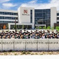 AlargegroupofgraduatesposeinregaliainfrontoftheNoordaCollegeofOsteopathicMedicinebuilding