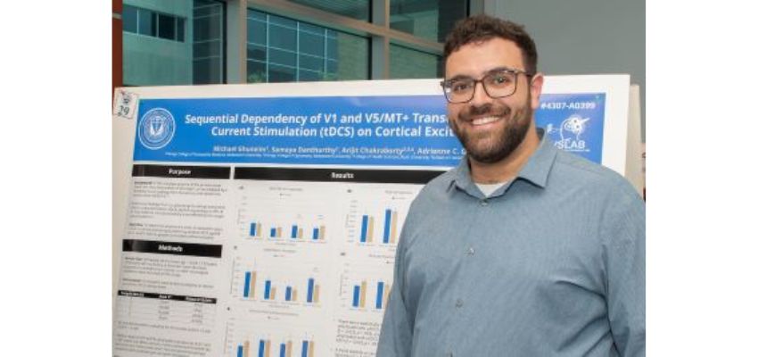 A student stands in front of a scientific research poster, smiling proudly at a presentation event.