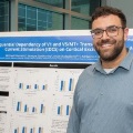 Astudentstandsinfrontofascientificresearchpostersmilingproudlyatapresentationevent