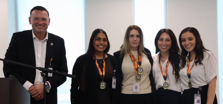A group of medical students and a faculty member pose together, all wearing badges and medals at a formal event.