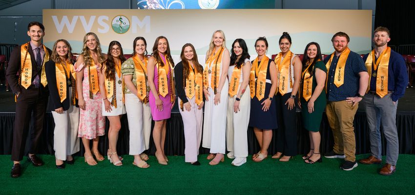 Students wearing honor sashes pose on stage at the West Virginia School of Osteopathic Medicine.