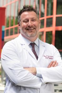 Dr. Peter Bidey stands outside with his arms folded, wearing his whitecoat
