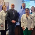 Agroupofmedicalstudentsandprofessionalsposeforaphotoinsideanofficesomewearingwhitecoats