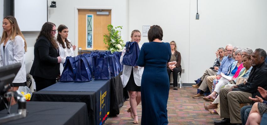A medical student hands out a remembrance gift as attendees watch from the audience.