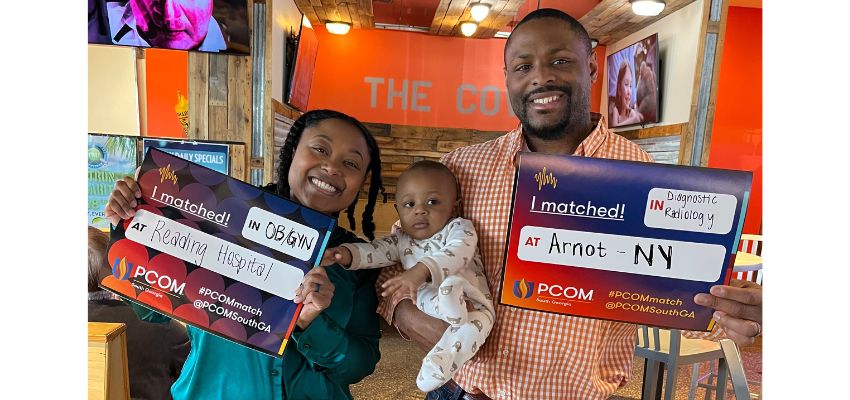 A smiling couple holds a baby and displays match signs indicating their residency placements in OB/GYN and Diagnostic Radiology.