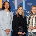Threewomenstandinfrontofabackdropataprofessionaleventoneholdinganawardplaque