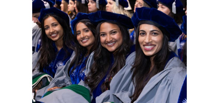 Graduating medical students smile in their academic regalia during a commencement ceremony.