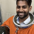 Amansmileswhilewearinganorangeastronauttrainingsuitholdingahelmet