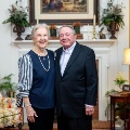 Anoldercouplestandssidebysideandsmilesinawarmlydecoratedlivingroomwithbookshelvesandtraditionalfurniture