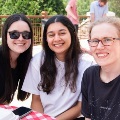 Threeyoungwomensitatanoutdoorpicnictablewithcheckeredclothsmilingonasunnyday