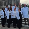 Agroupofstudentsandfacultyinwhitecoatsposetogetheronthestepsofalargestonebuildinglikelyagovernmentorhistoricsite