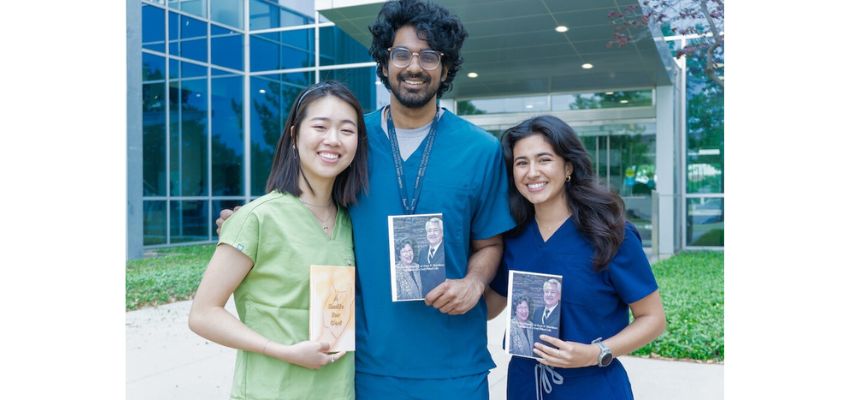 Three smiling students in scrubs hold awards and framed photos while standing outside a university building.