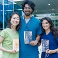 Threesmilingstudentsinscrubsholdawardsandframedphotoswhilestandingoutsideauniversitybuilding
