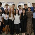 AdiversegroupofstudentsdressedinbusinesscasualclothingposetogetherunderaballoonarchwithVCOMlettersbehindthem